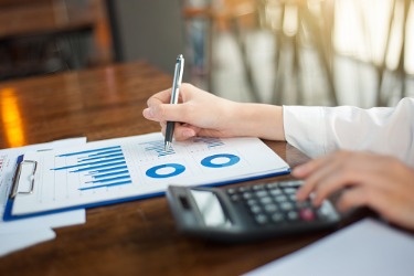 woman with clipboard writing on graph near calculator